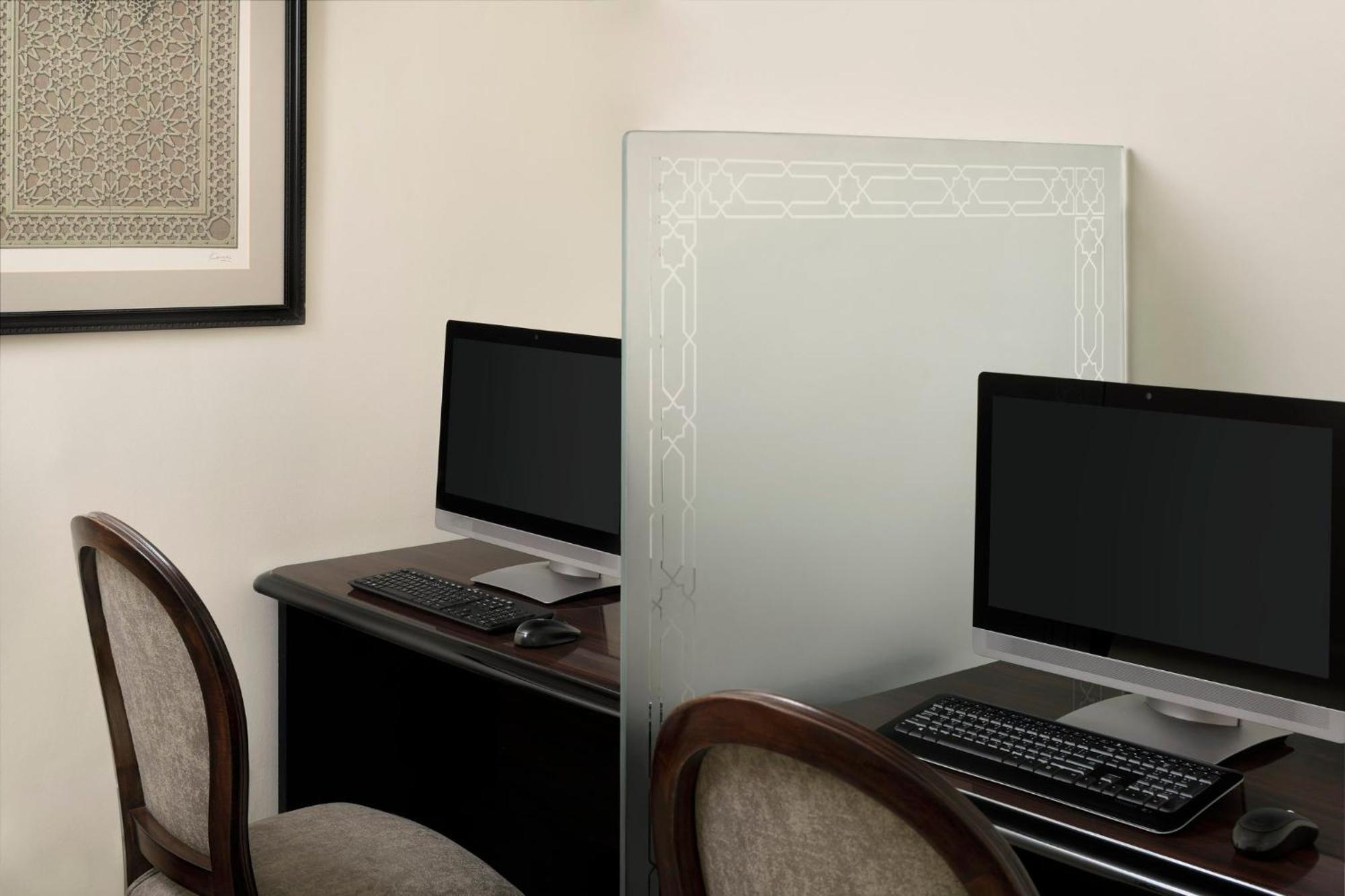 Intercontinental Dar Al Iman Madinah By Ihg Hotell Medina Exteriör bild The photo shows a small office or workspace area featuring two computer stations. Each station has a black monitor, a keyboard, and appears to be set up on a dark wooden desk. A translucent glass partition is placed between the two workstations, prov