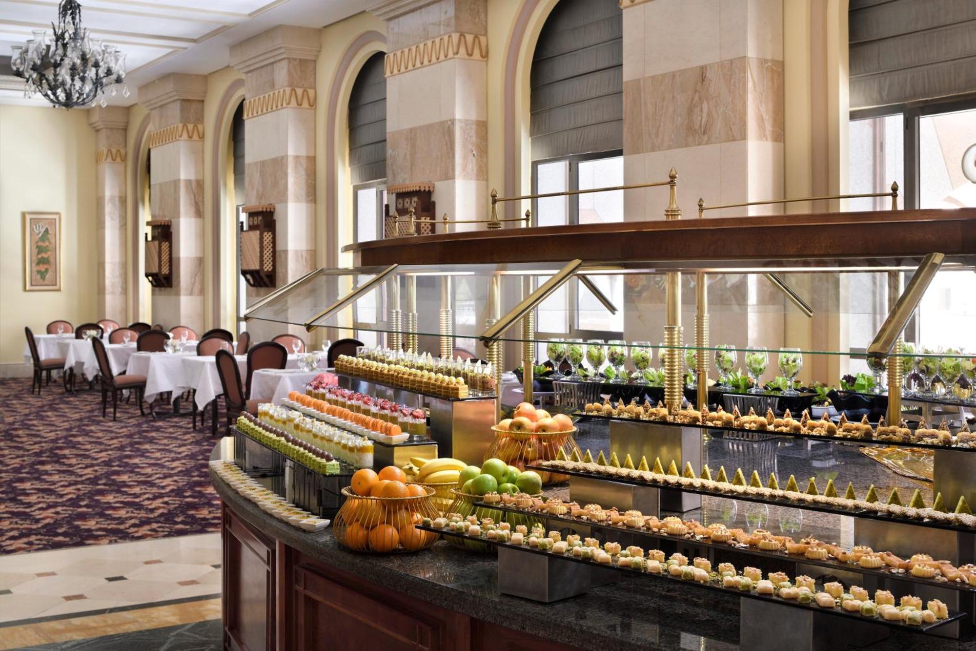 Intercontinental Dar Al Iman Madinah By Ihg Hotell Medina Exteriör bild The photo depicts an elegant dining area featuring a buffet-style display. In the foreground, a beautifully arranged buffet counter showcases an array of desserts, including miniature pastries and colorful fruit. The setting has a sophisticated ambia