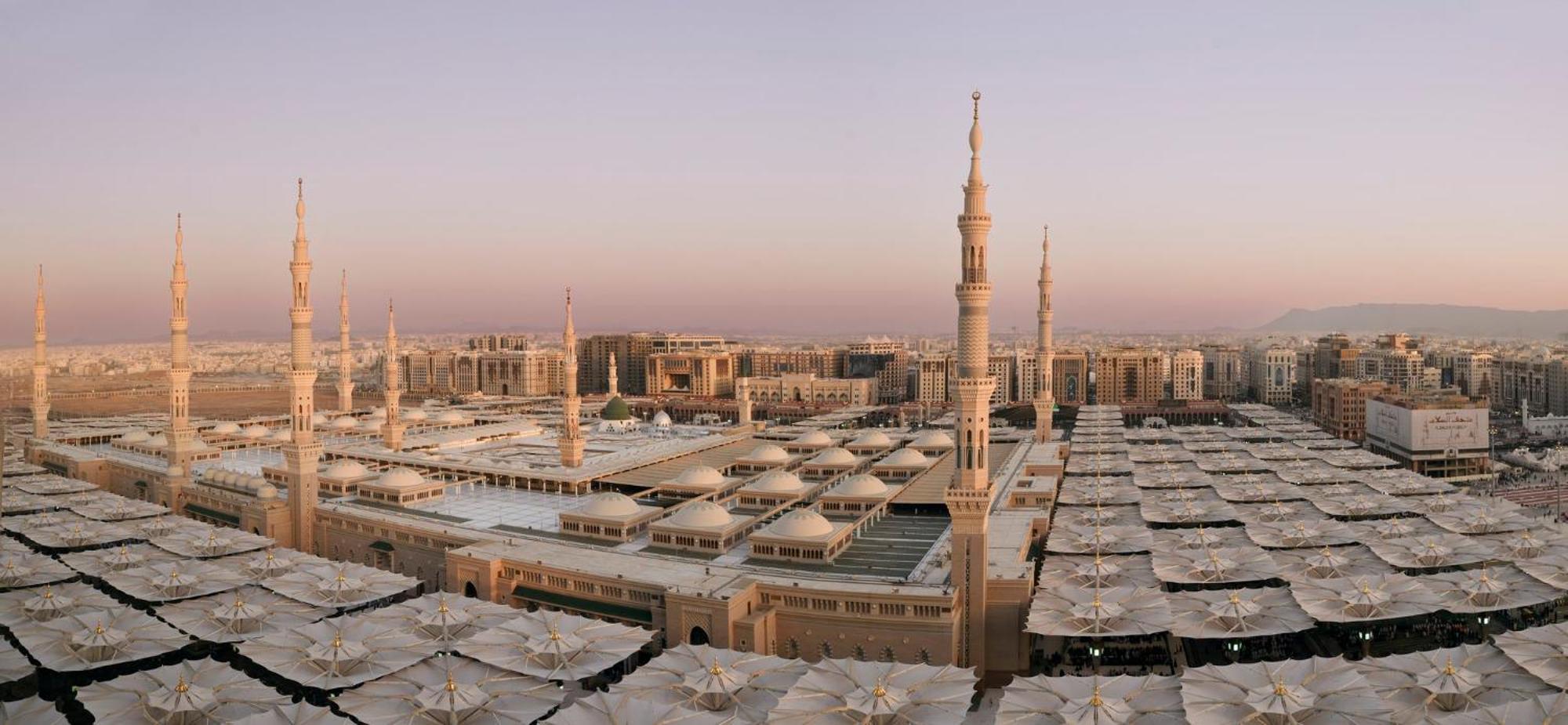 Intercontinental Dar Al Iman Madinah By Ihg Hotell Medina Exteriör bild The photo shows an aerial view of the Al-Masjid an-Nabawi, or the Prophet's Mosque, located in Medina, Saudi Arabia. The mosque features distinct minarets, large white domes, and expansive open areas with large umbrellas that provide shade for visito