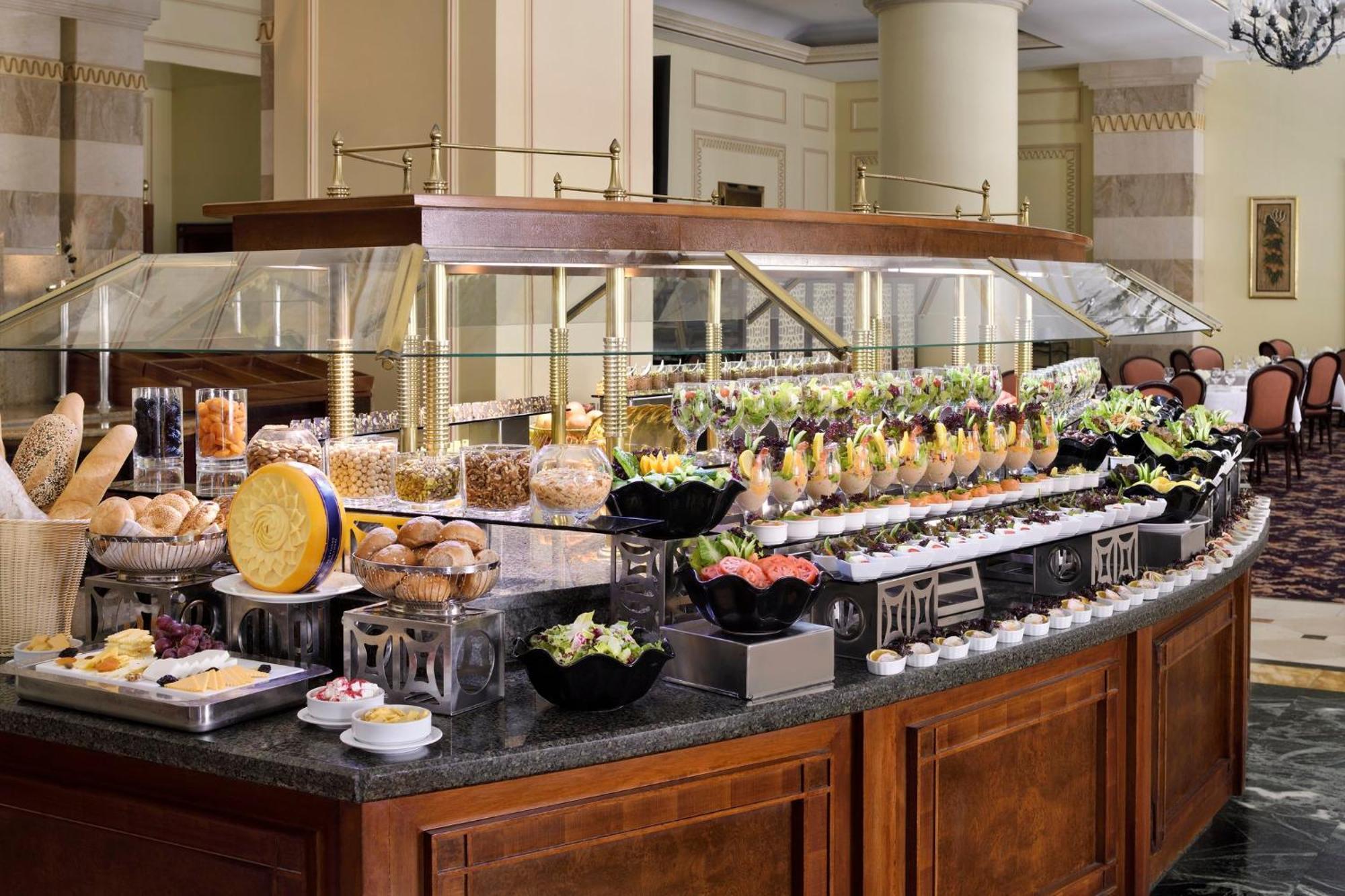 Intercontinental Dar Al Iman Madinah By Ihg Hotell Medina Exteriör bild The photo shows an elegantly arranged buffet with a variety of food items. There is a large, curved wooden display with glass covers, showcasing an assortment of dishes. These include different types of breads and rolls, salads, garnishes, and desser