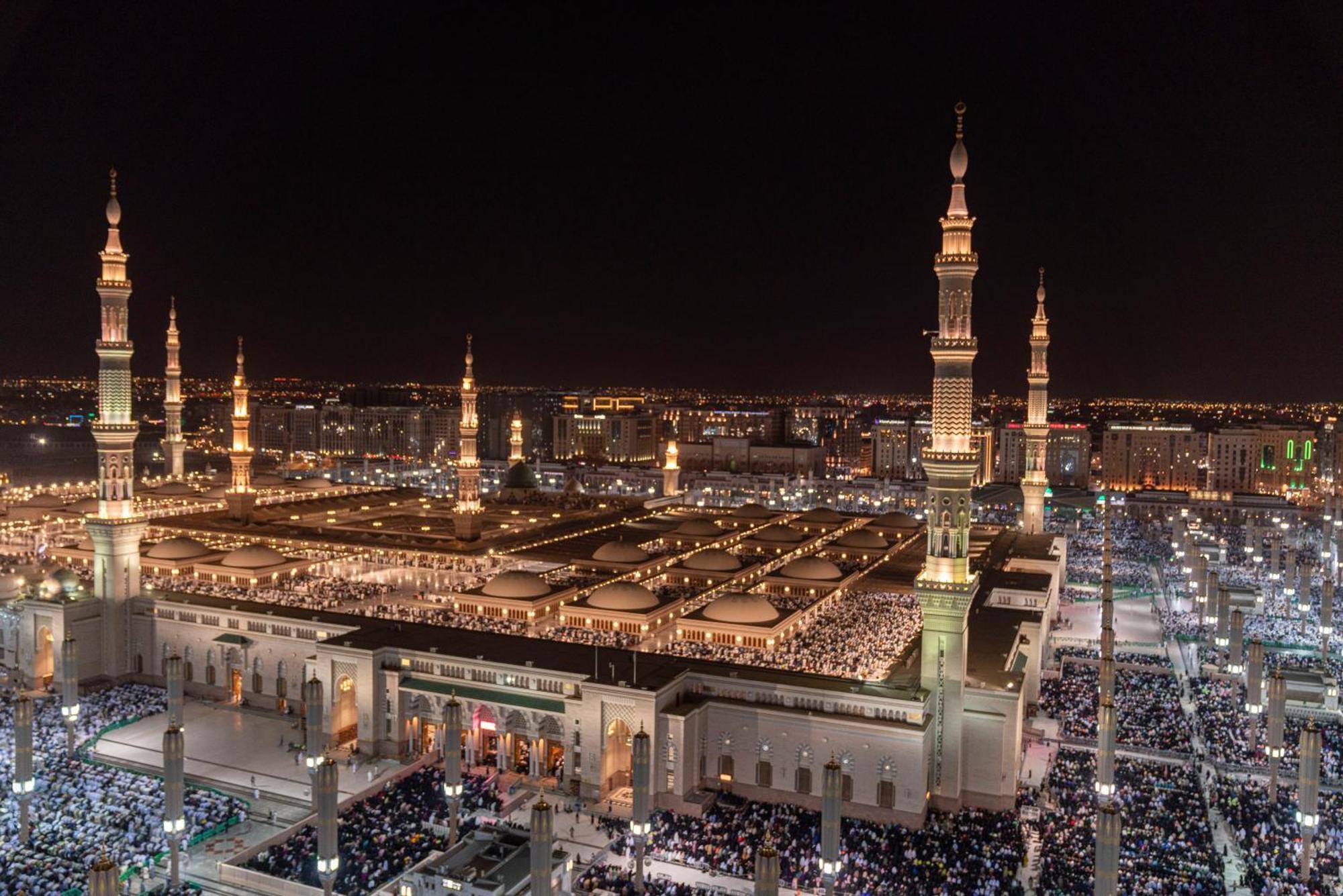 Intercontinental Dar Al Iman Madinah By Ihg Hotell Medina Exteriör bild The photo shows a panoramic view of a large mosque complex illuminated at night. It features tall minarets with lights, a vast courtyard filled with people, and a beautifully lit architectural design. The overall ambiance suggests a significant space