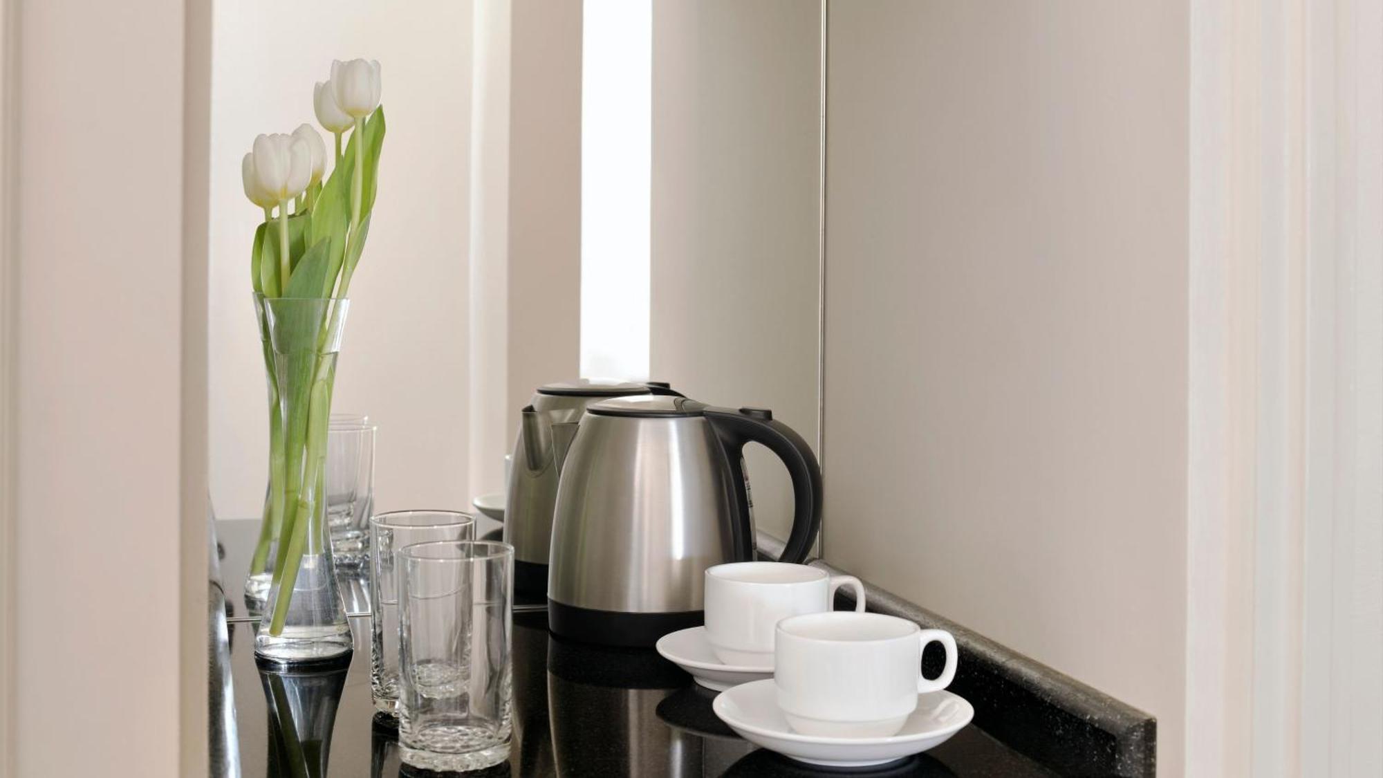 Intercontinental Dar Al Iman Madinah By Ihg Hotell Medina Exteriör bild The photo depicts a neatly arranged beverage area. In the foreground, there are two white coffee cups on small saucers. Next to them, there are two clear drinking glasses. In the background, there is a silver electric kettle, which is positioned next