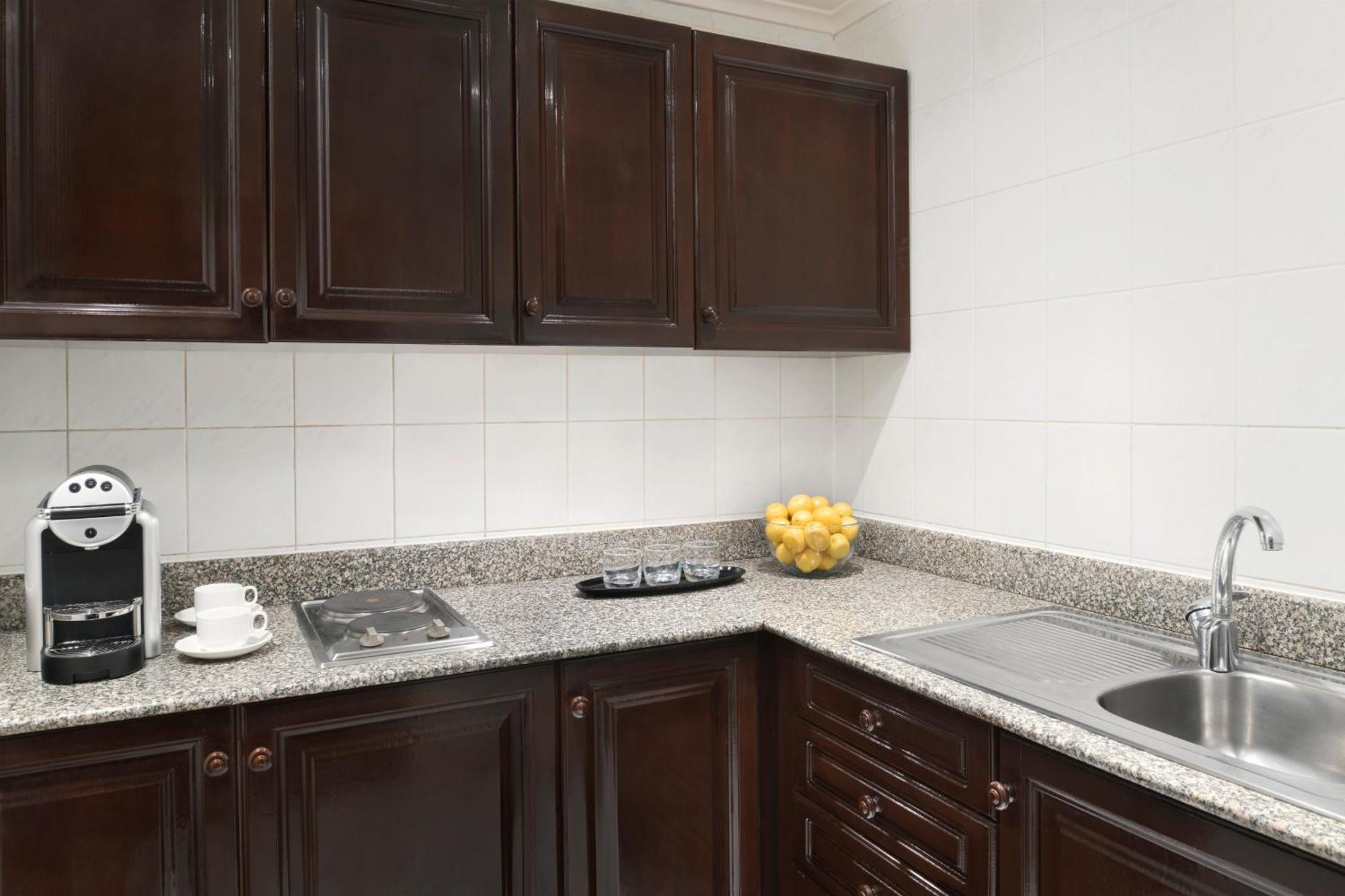 Intercontinental Dar Al Iman Madinah By Ihg Hotell Medina Exteriör bild The photo shows a kitchen with dark wooden cabinetry and a light-colored countertop. There are a few appliances visible, including a coffee machine and a stovetop with burners. To the right, there is a sink, and a bowl of yellow lemons is placed on t