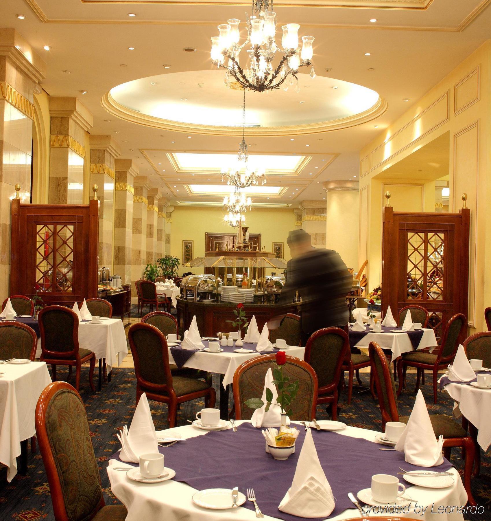 Intercontinental Dar Al Iman Madinah By Ihg Hotell Medina Restaurang bild The photo depicts an elegant restaurant interior. It features round tables covered with white tablecloths, each set with plates, cutlery, and folded napkins arranged into triangles. The space has a warm, inviting atmosphere with a mix of decorative e